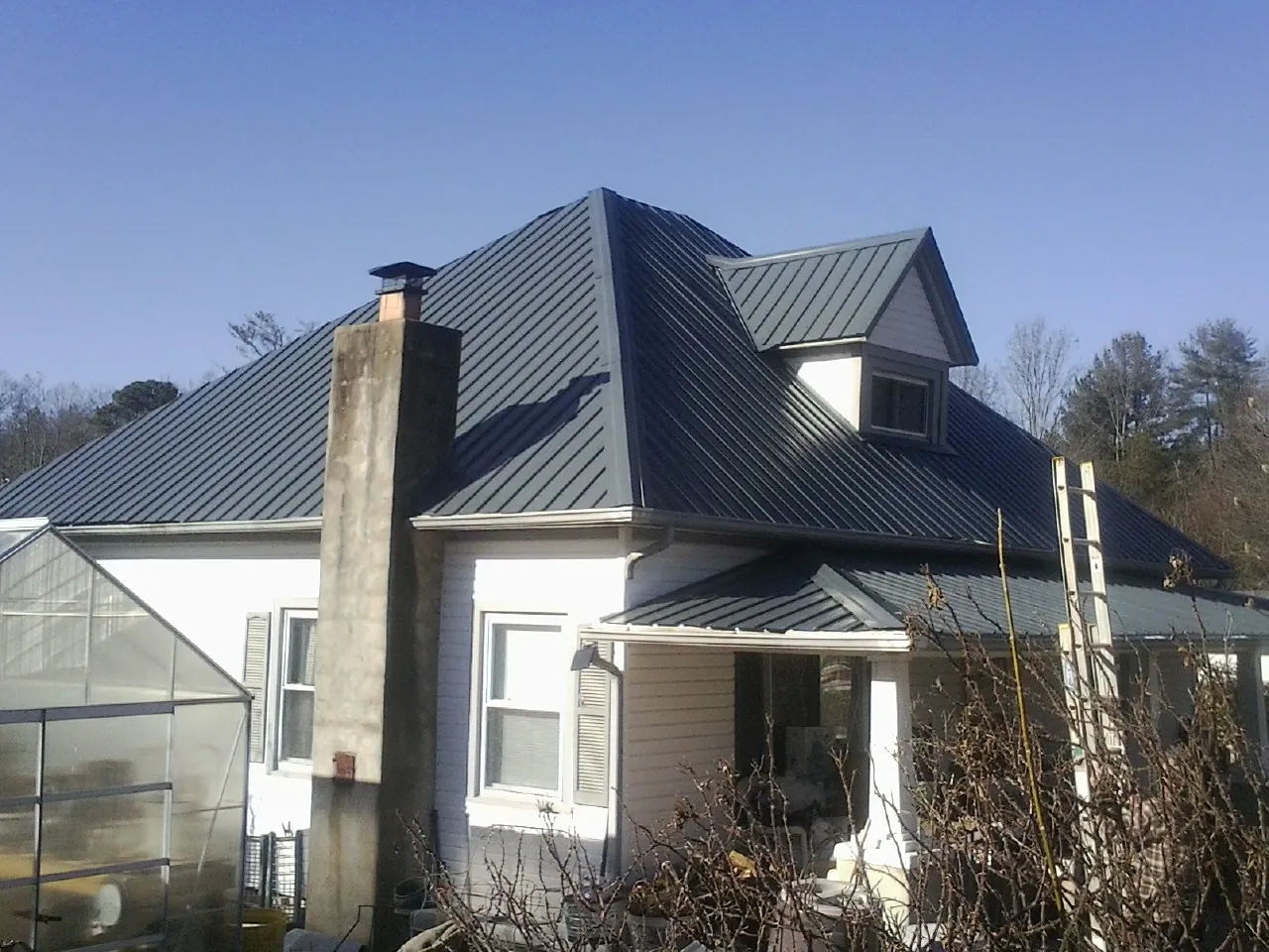 Dark blue standing seam metal roof on a white farmhouse with dormer — Slate & Tile Roof Repair by Roofing Brothers in Arden