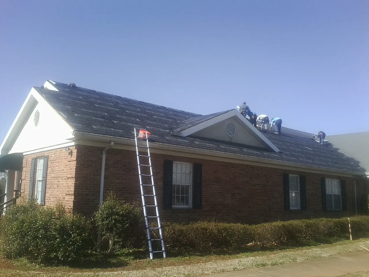 Crew tearing shingles off a brick ranch roof with a ladder set — Metal Roof Repair work by our crew in Arden
