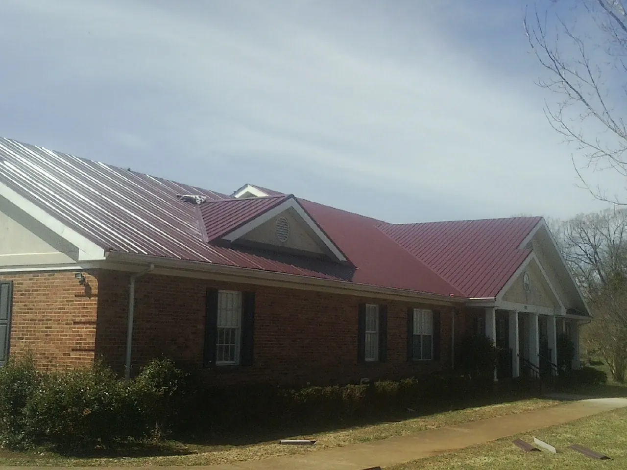 Red metal roof with gabled entries on a long brick building, from a Hail Damage Roof Repair job in Arden