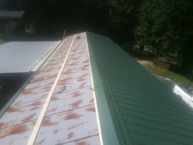 Old rusted panels beside newly installed green metal roofing — Wind Damage Roof Repair by Roofing Brothers in Arden