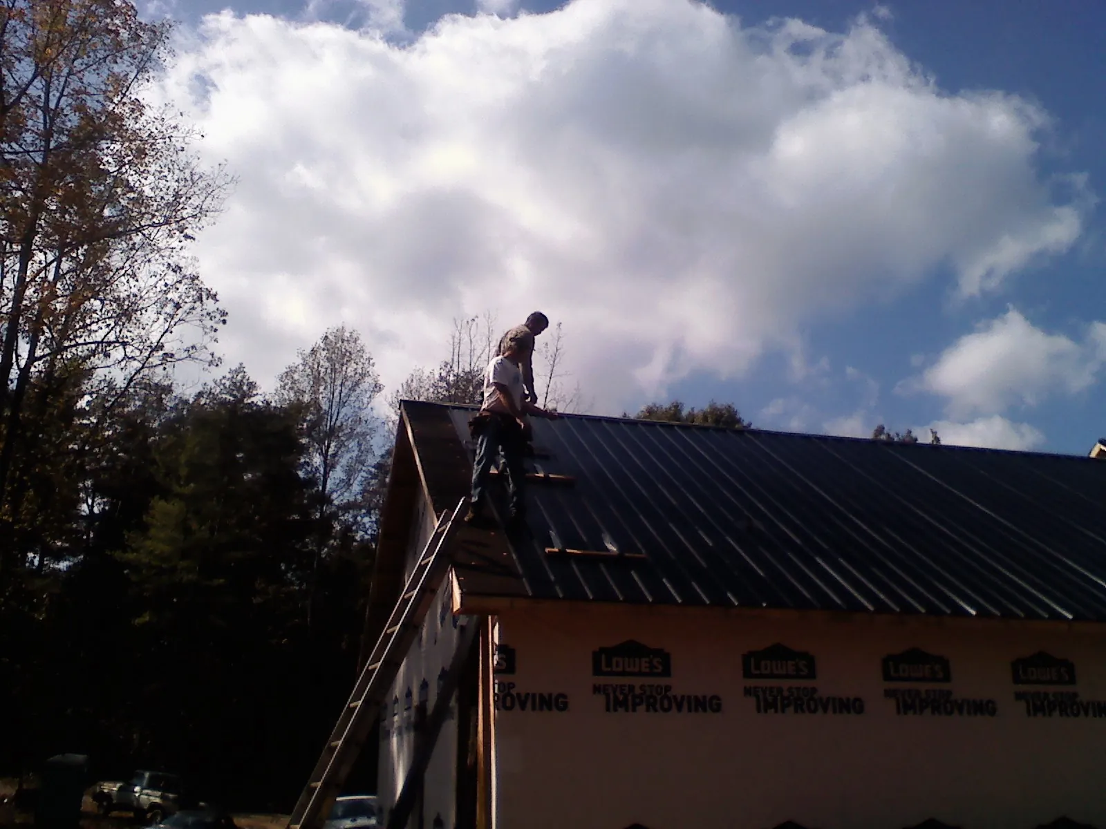 Roofer fastening dark metal panels high against a cloudy sky, from a Roof Inspection job in Arden