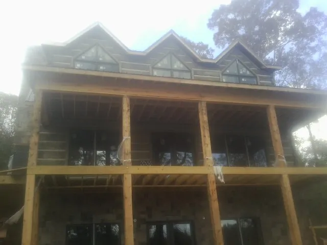 Dormers and porch framing on a large log home under construction — Roof Coating work by our crew in Arden