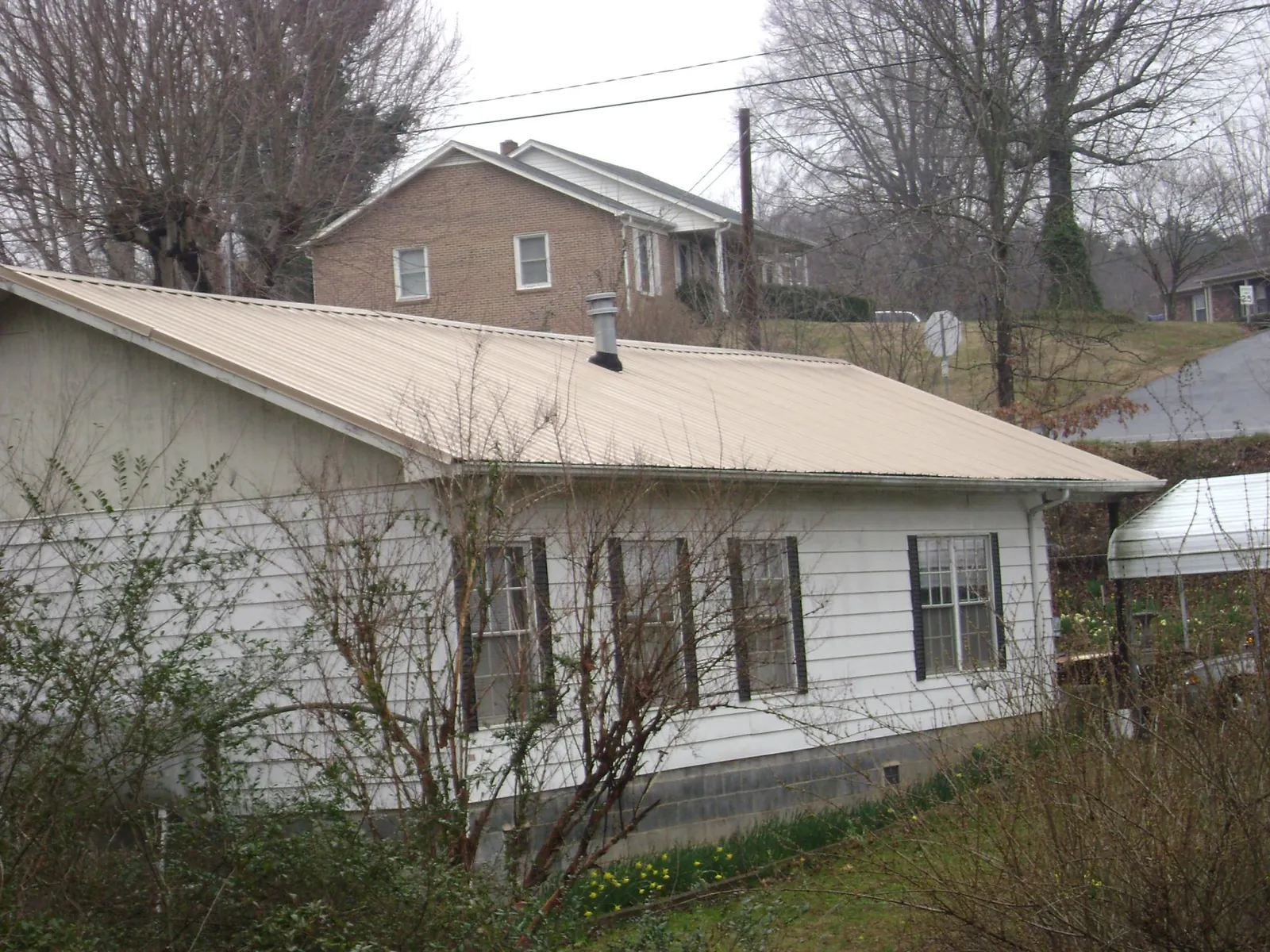 Tan metal roof on a white sided house set into a hillside — Commercial Roofing by Roofing Brothers in Arden