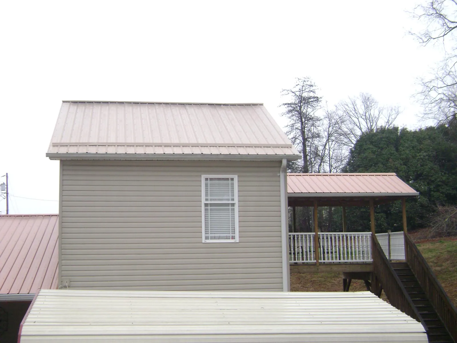 Tan metal roofs on a two story addition and attached porch, from a Roof Replacement job in Arden